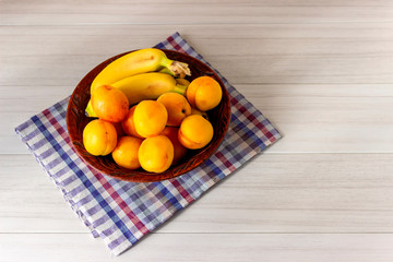 Bananas and apricots lie in a plate on a white table.