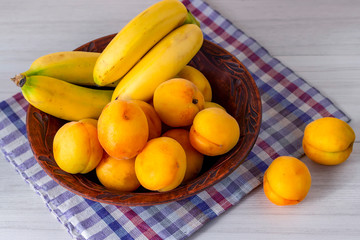 Bananas and apricots lie in a plate on a white table.