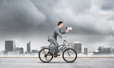 Obraz premium Businessman with megaphone in hand on bike
