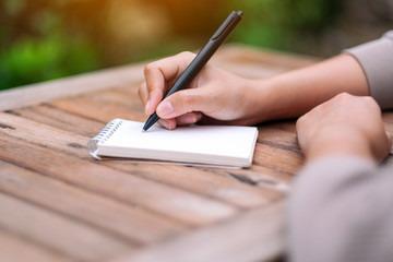 Closeup image of a woman writing on blank notebook on wooden table in the outdoors