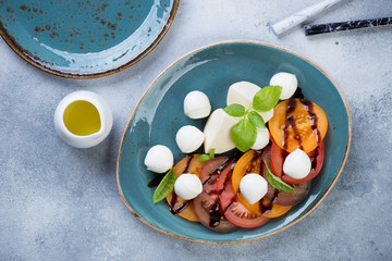 Turquoise plate with caprese salad over light-blue stone background, view from above, horizontal shot