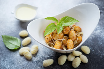 Bowl of potato gnocchi with red pesto sauce, grated parmesan and green basil over grey stone surface