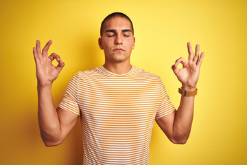 Young handsome man wearing striped t-shirt over yellow isolated background relax and smiling with eyes closed doing meditation gesture with fingers. Yoga concept.