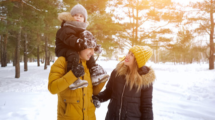 Happy young family, mom, son and dad are walking together in winter park, copyspace. Woman is showing something by her hand to her husband and son.