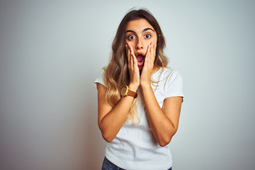 Young beautiful woman wearing casual white t-shirt over isolated background afraid and shocked, surprise and amazed expression with hands on face
