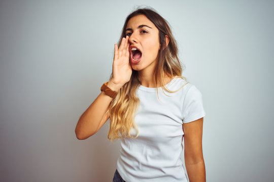 Young beautiful woman wearing casual white t-shirt over isolated background shouting and screaming loud to side with hand on mouth. Communication concept.