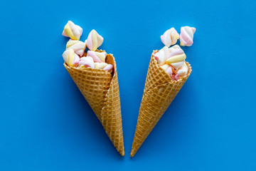 Sweet desserts. Marshmallows in ice cream waffle cone on blue background top view