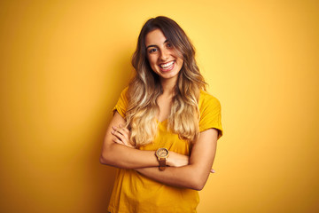 Young beautiful woman wearing t-shirt over yellow isolated background happy face smiling with crossed arms looking at the camera. Positive person.