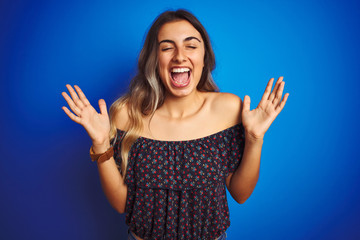 Fototapeta na wymiar Young beautiful woman wearing floral t-shirt over blue isolated background celebrating crazy and amazed for success with arms raised and open eyes screaming excited. Winner concept