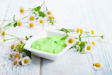 green cosmetis cream with chamomile flowers on white wooden table