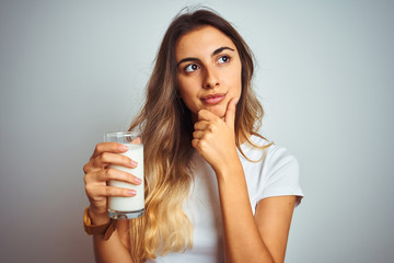 Young beautiful woman drinking a glass of milk over white isolated background serious face thinking...