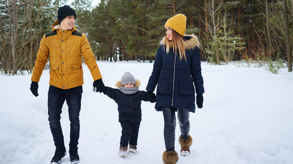 Fototapeta na wymiar Portrait of happy family walk in winter day. Mom and dad are holding hands their little son in winter park, copy space. Family lovely moments.