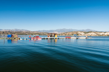Fototapeta na wymiar Cachuma Lake marina with a variety of fishing and pontoon boats, paddleboats, kayaks, and rowboats, blue sky and mountains on background. Cachuma Lake Recreation Area, Santa Barbara County