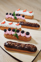 Traditional French dessert. Eclair with cream, chocolate icing, strawberries, cherry, mint on wooden background close up