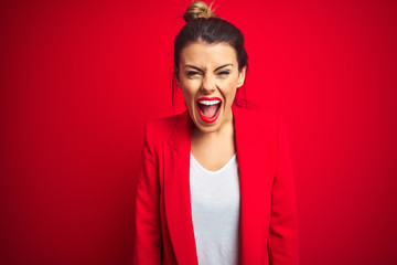 Young beautiful business woman standing over red isolated background angry and mad screaming frustrated and furious, shouting with anger. Rage and aggressive concept.