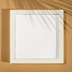 White photo frame on a beige background with a palm leaf shadow