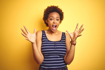 Beauitul african american woman wearing summer t-shirt over isolated yellow background celebrating crazy and amazed for success with arms raised and open eyes screaming excited. Winner concept