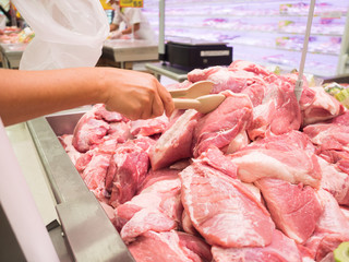 Close up woman buyer hand use tong to clamping fresh pork at fresh food zone in the supermarket.Customer buying red meat in the fresh meal shop.Choose to buy fresh food concept.
