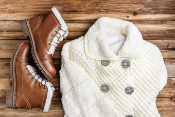 Warm outerwear for women. Knitted white coat and brown boots with fur.