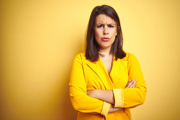 Young beautiful brunette woman wearing elegant dress over yellow isolated background skeptic and nervous, disapproving expression on face with crossed arms. Negative person.