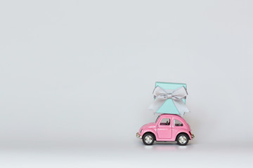 Pink retro toy car delivering gift box on roof on white background. Valentine day February 14, International women day 8 March, mother day, birthday celebrate. Copy space, mockup, template, minimal