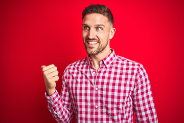 Fototapeta premium Young handsome man over red isolated background smiling with happy face looking and pointing to the side with thumb up.