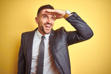 Young handsome business man over yellow isolated background very happy and smiling looking far away with hand over head. Searching concept.