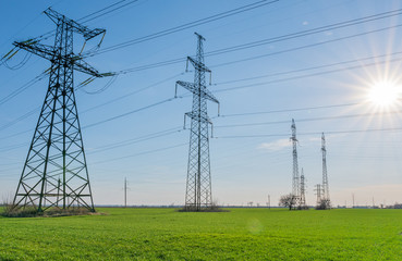 High voltage lines and power pylons and a green agricultural landscape on a sunny day.