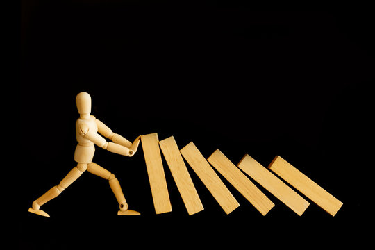 Wooden man model or businessman against and stopping the risk of falling domino effect isolated on dark background. Business crisis,risk, management,intervention,solution and prevention conceptual