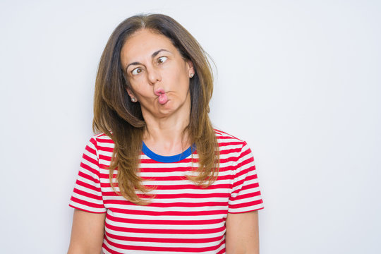 Middle age senior woman standing over white isolated background making fish face with lips, crazy and comical gesture. Funny expression.