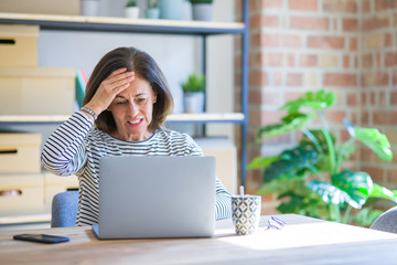 Middle age senior woman sitting at the table at home working using computer laptop stressed with...