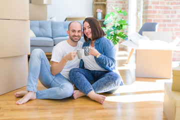 Young couple sitting on the floor of new house arround cardboard boxing, relaxing from moving drinking a cup of coffee smiling very happy