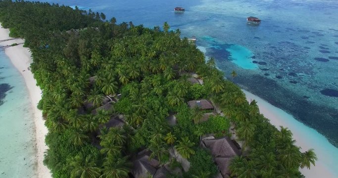 4K Aerial drone view of a luxury island resort on exotic white sand beach and over-water villas in Maldives. Blue lagoon and palm trees. Travel agency and trip advisor concept