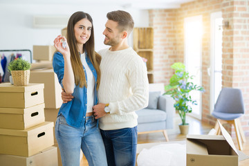 Young couple moving to a new home, hugging in love showing keys of new apartment smiling very happy