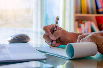 Business man hand writing and signing cheque book with laptop computer on the wooden table at...