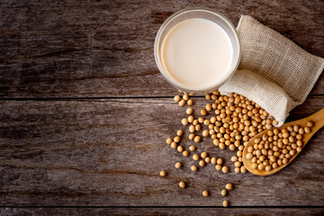 Closeup soybeans in wooden spoon and glass of soy milk isolated on old wooden table background. Vintage style. Top view.