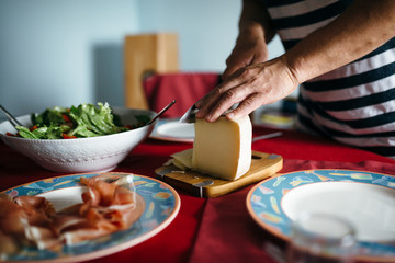 Fototapeta na wymiar A dining table served with a bowl of salad, spanish jamon and a man slicing up a piece of cheese