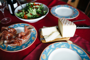 A dining table served with a bowl of salad, spanish jamon and sliced cheese