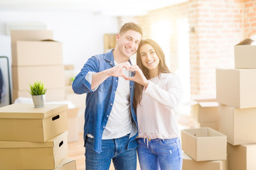 Fototapeta na wymiar Beautiful young couple moving to a new house smiling in love showing heart symbol and shape with hands. Romantic concept.