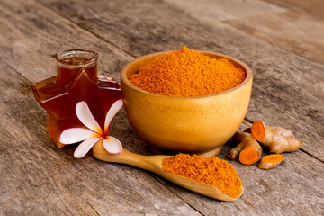Turmeric powder in wooden bowl and spoon with curcuma root,honey and plumeria flower isolated on old wood table background. Natural medical plant ,Homemade ingredients beauty products and spa concept 