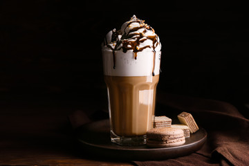 Glass of tasty frappe coffee with sweets on wooden table