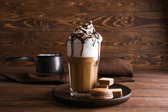 Glass of tasty frappe coffee with sweets on wooden table
