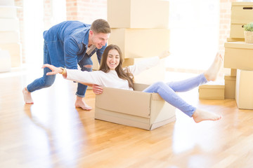 Beautiful young couple smiling in love having fun riding inside a cardboard box, celebrating moving to a new home