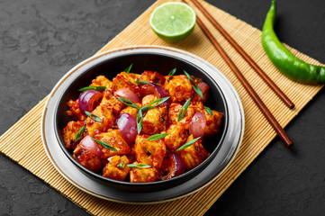Schezwan Paneer in black bowl at dark slate background. Schezwan Paneer is indo-chinese cuisine dish with deep fried Paneer cheese, onion and Schezwan Sauce
