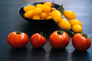 Top view of yellow and red cherry tomatoes in bowl on black wooden background