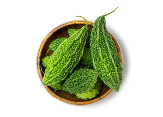 Closeup fresh bitter gourd (cucumber, Momordica Charantia) in wooden bowl isolated on white background.  Clipping path. Top view. - obrazy, fototapety, plakaty