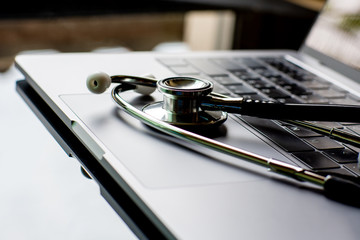 Closeup medical stethoscope and computer notebook isolated on dark  office desk background. Tetehealth,medic tech,ehealth,online medical,medical network,support and maintenance concept.