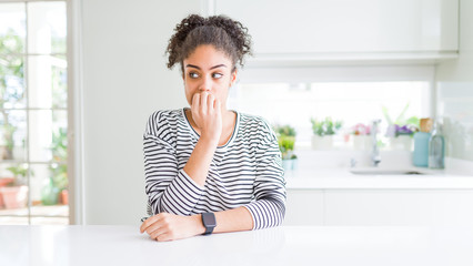 Beautiful african american woman with afro hair wearing casual striped sweater looking stressed and nervous with hands on mouth biting nails. Anxiety problem.