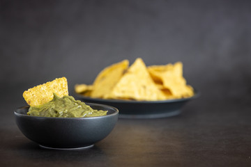 Green Guacamole with nachos in bowl on dark background