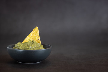 Green Guacamole with nachos in bowl on dark background